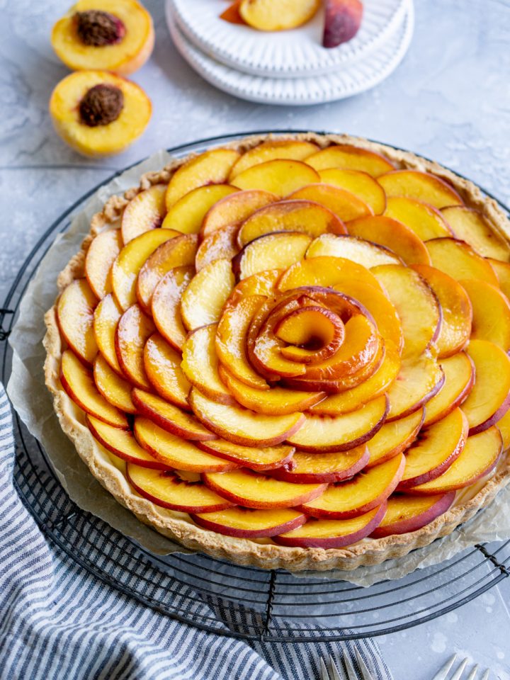 Side view of a peach tart with sliced peaches on a plate in the background
