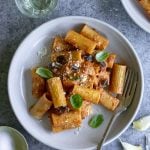 Eggplant pasta in a plate surrounded by garlic and a glass of white wine