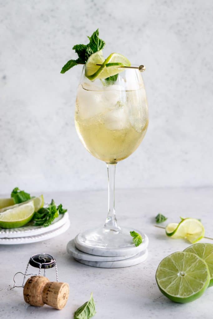 A hugo cocktail in a wine glass garnished with mint and lime