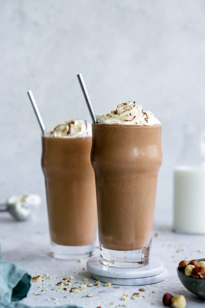 Two nutella milkshakes with straws and a jar of milk in the background