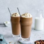 Two nutella milkshakes in tall glasses with a bowl of hazelnuts and a napkin to the side