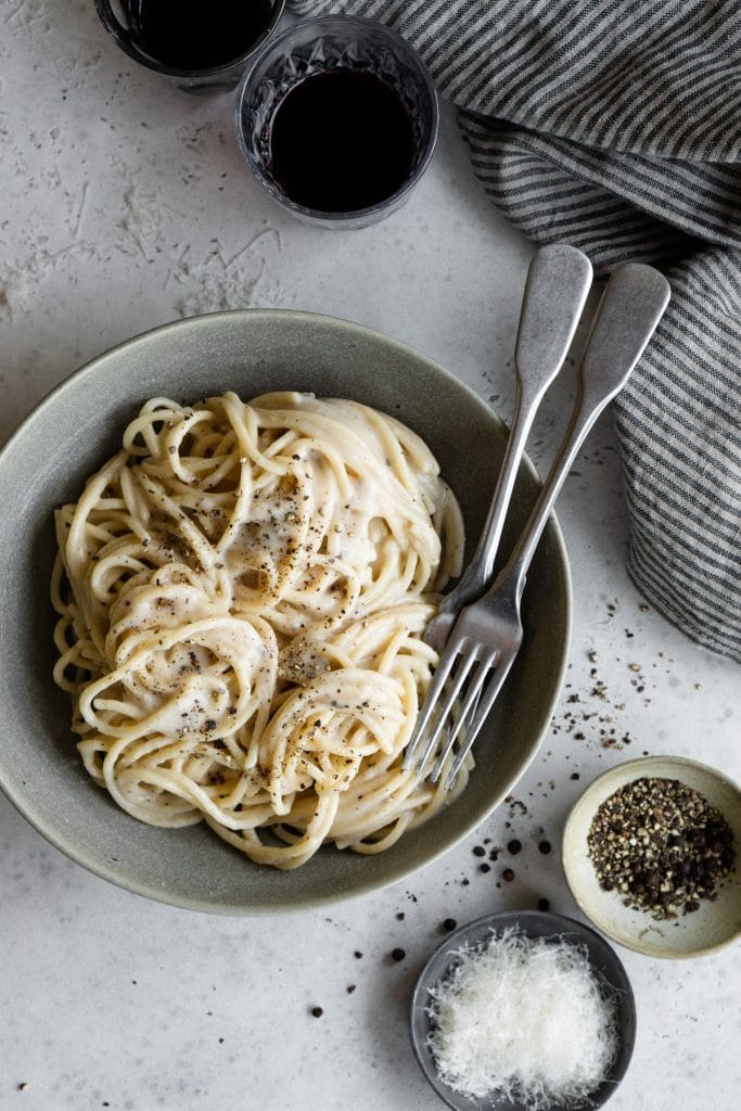 Bowl of traditional cacio e pepe spaghetti with 2 glasses of red wine above it