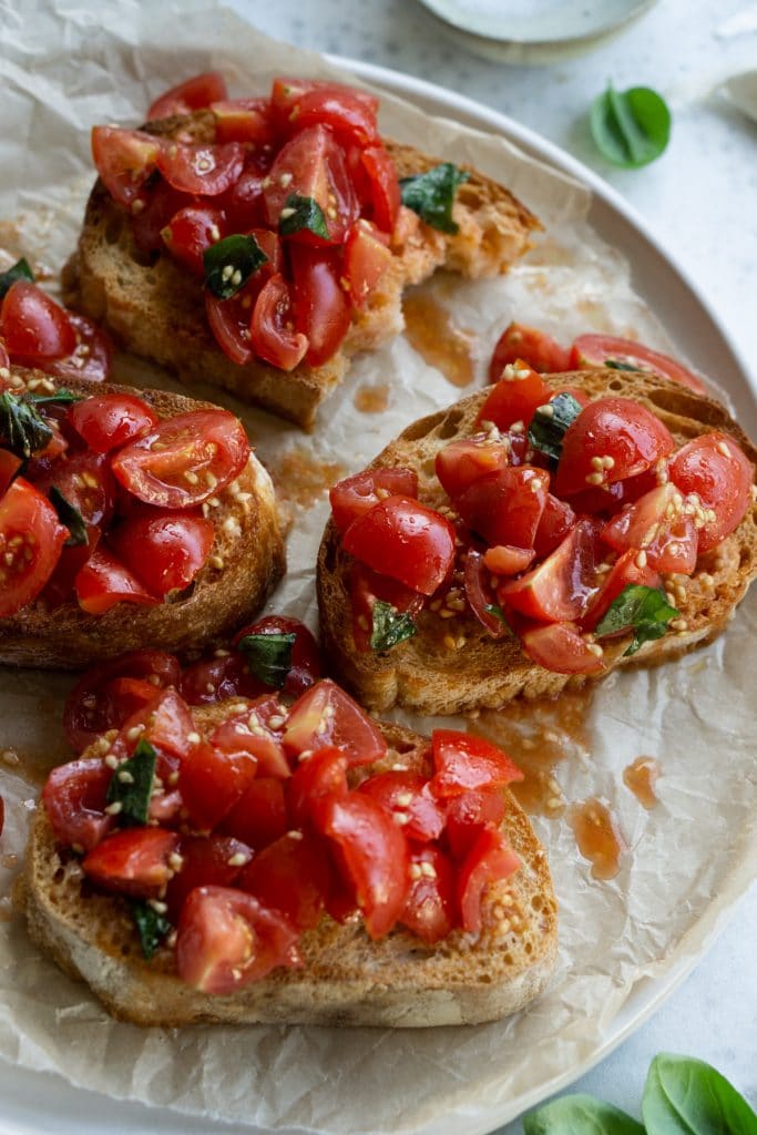 Tomato bruschetta on a plate, surrounded by pieces of basil