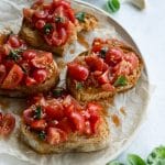 Classic tomato bruschetta on a plate with salt, garlic and basil in the background