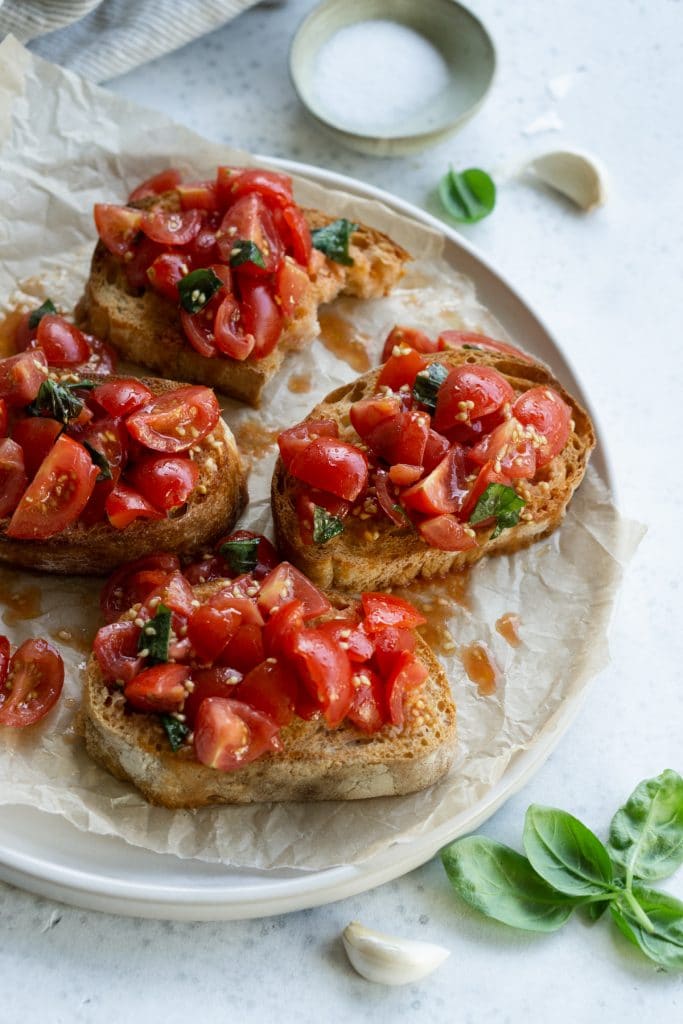 Classic tomato bruschetta on a plate with salt, garlic and basil in the background