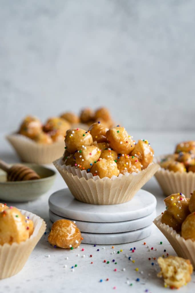 Struffoli in a muffin liner topped with sprinkles propped up by three coasters