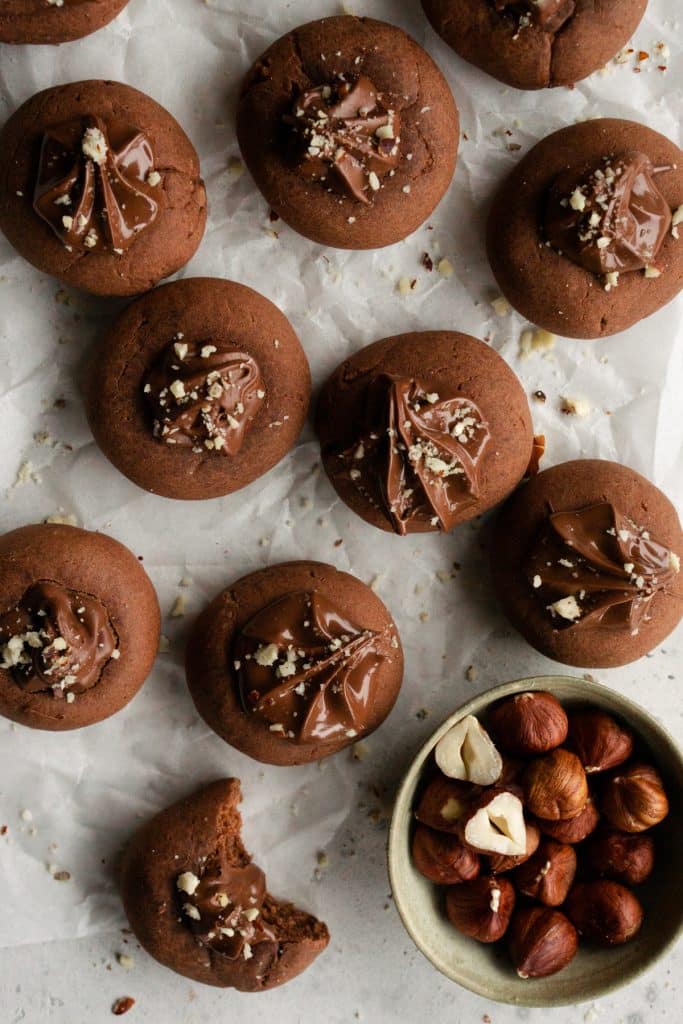 Nutella cookies on parchment paper and a bowl of hazelnuts