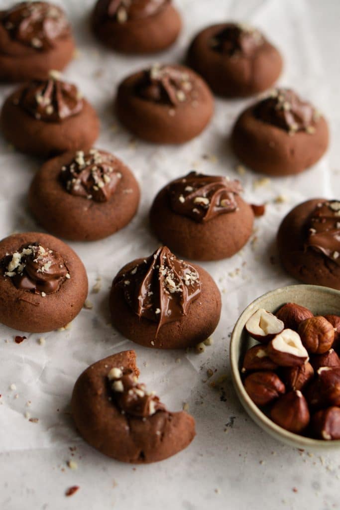 Cluster of 3-ingredient nutella cookies with a bowl of hazelnuts to the side