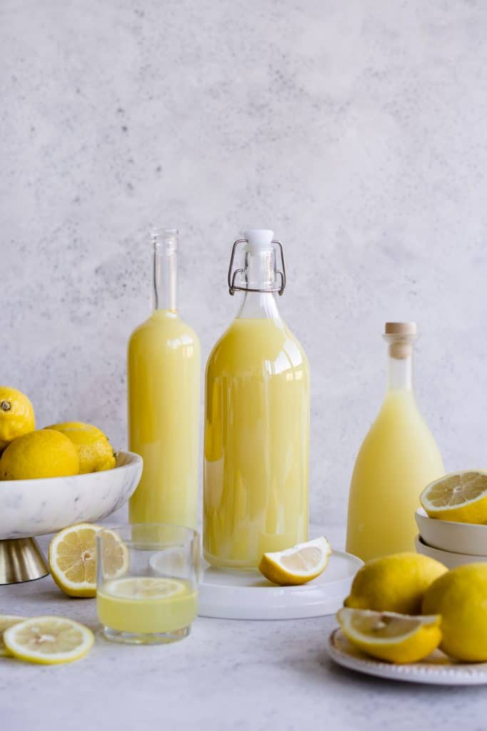 Three bottles of limoncello surrounded by bowls and plated of lemons