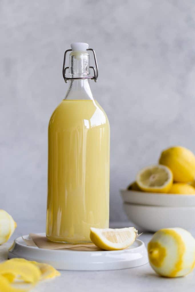 One bottle of limoncello on a white plate with a bowl of lemons in the background