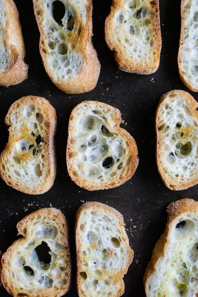 Slices of baked crostini on a black sheet pan