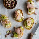Five burrata crostini with mortadella and a bowl of pistachios