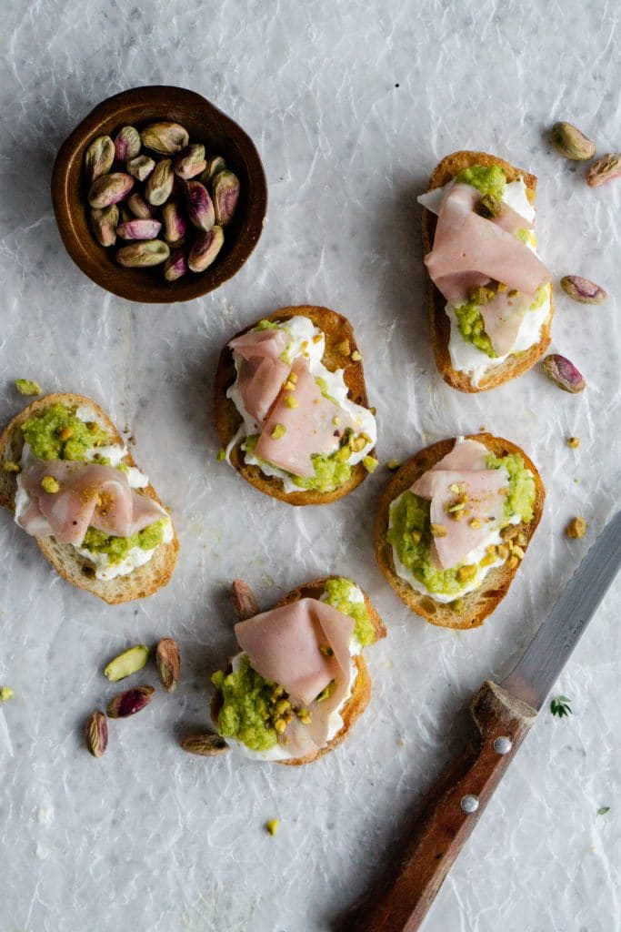 Five burrata crostini with mortadella and a bowl of pistachios