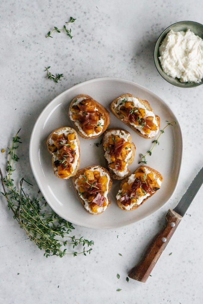 Plate of butternut squash crostini with a small dish of ricotta to the side