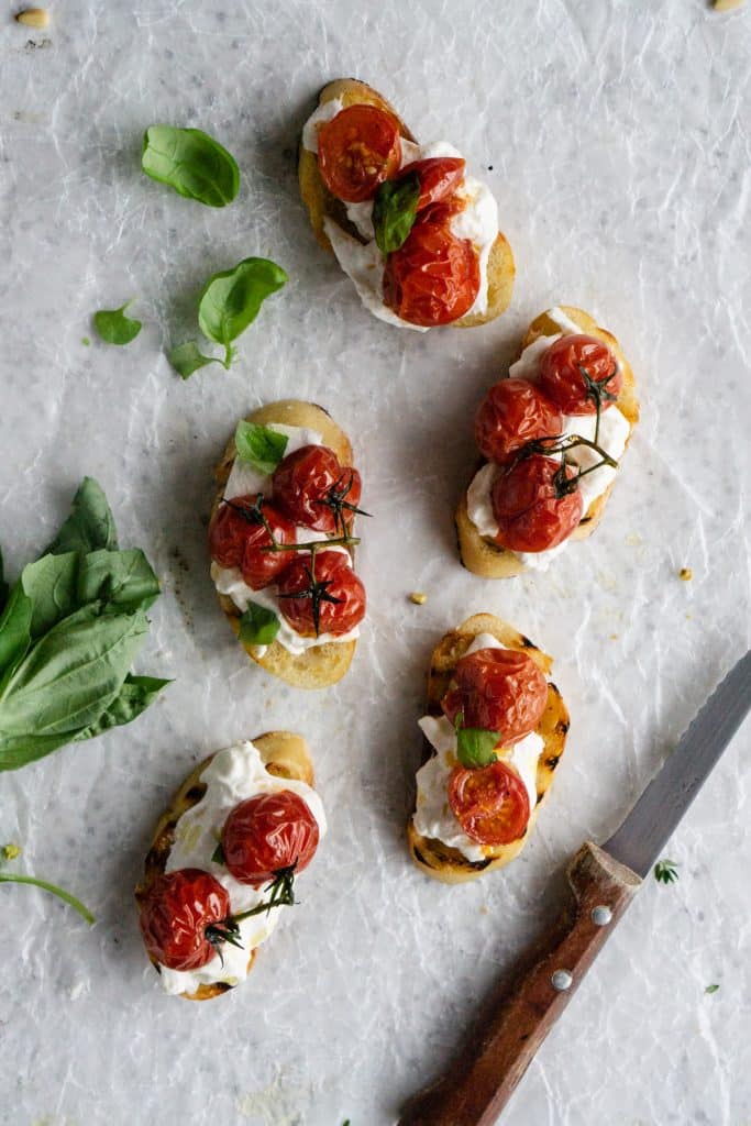 Roasted tomato crostini topped with fresh basil and a knife to the side