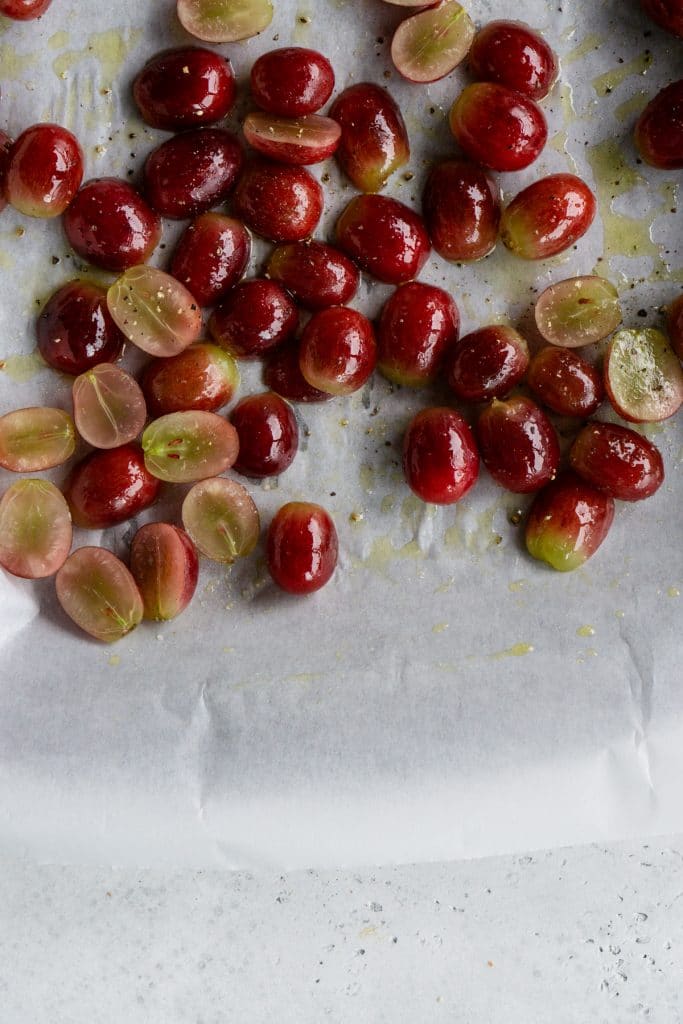 Fresh grapes cut in half on a baking sheet drizzled with olive oil, salt and pepper
