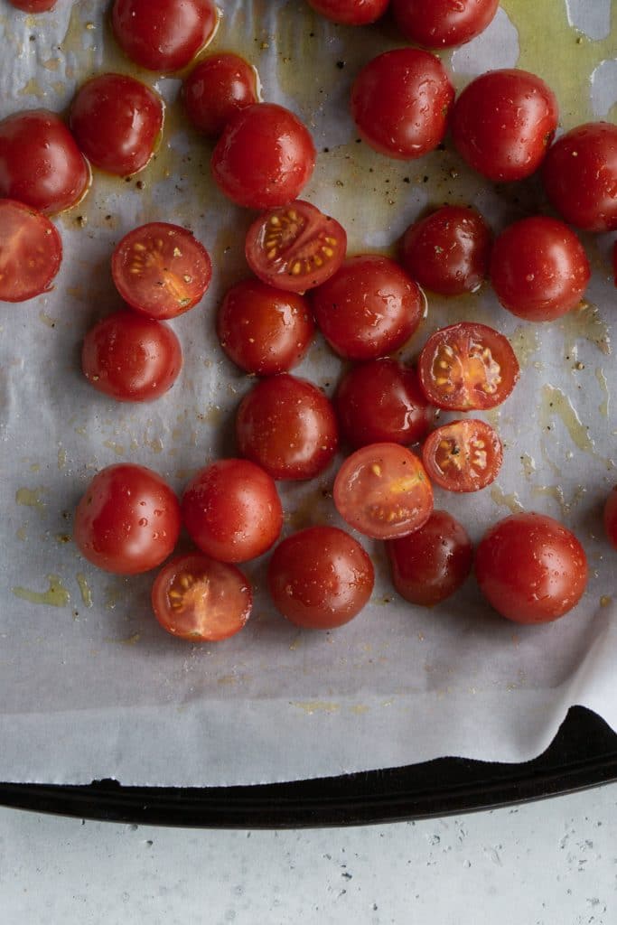 Raw tomatoes on a baking sheet drizzled with olive oil, salt and pepper