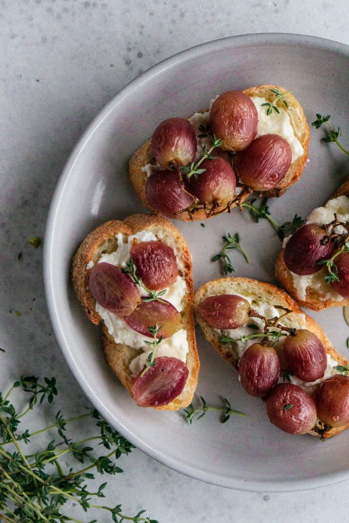 Roasted grape crostini in a grey plate with fresh thyme to the side