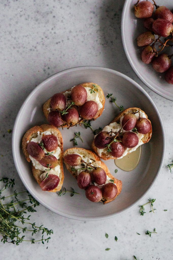 Plate of roasted grape crostini with another plate of roasted grapes next to it