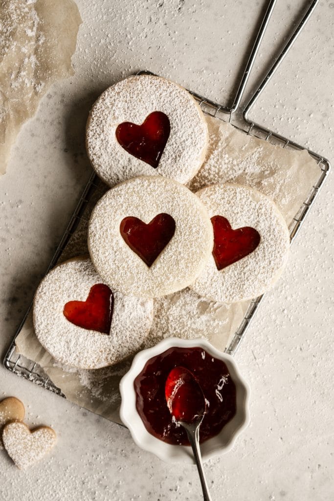 Four jam cookies on a metal tray with a small bowl of jam
