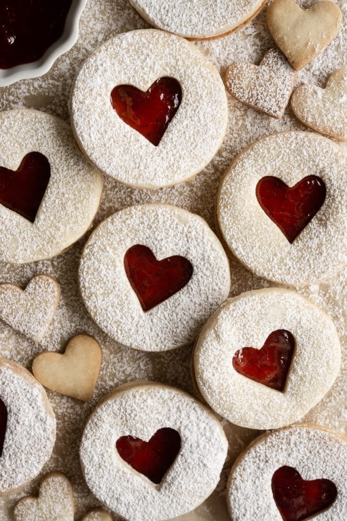 Overhead view of jam cookies with a heart cutout on parchment paper