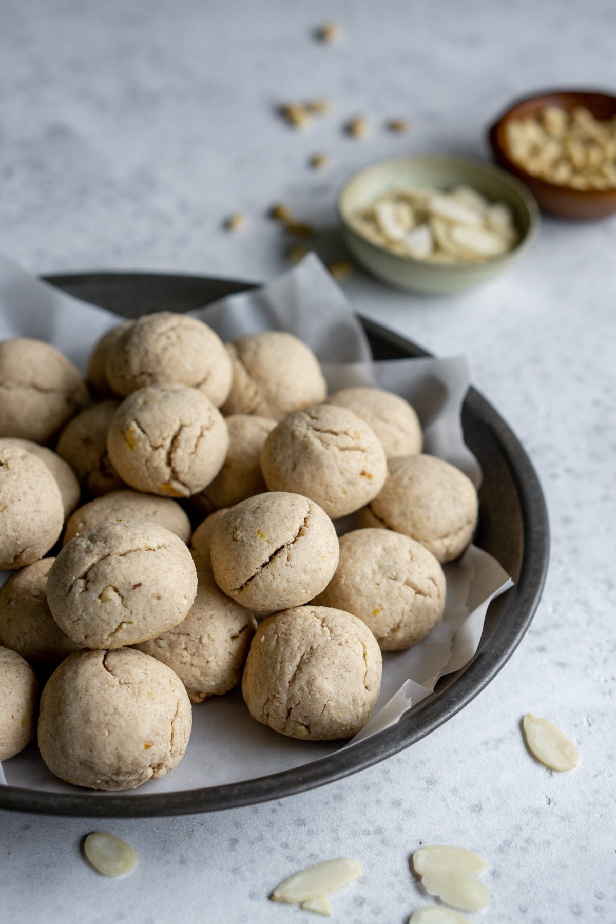 Fave dei morti in a gray circular pan with almonds and pine nuts in the background