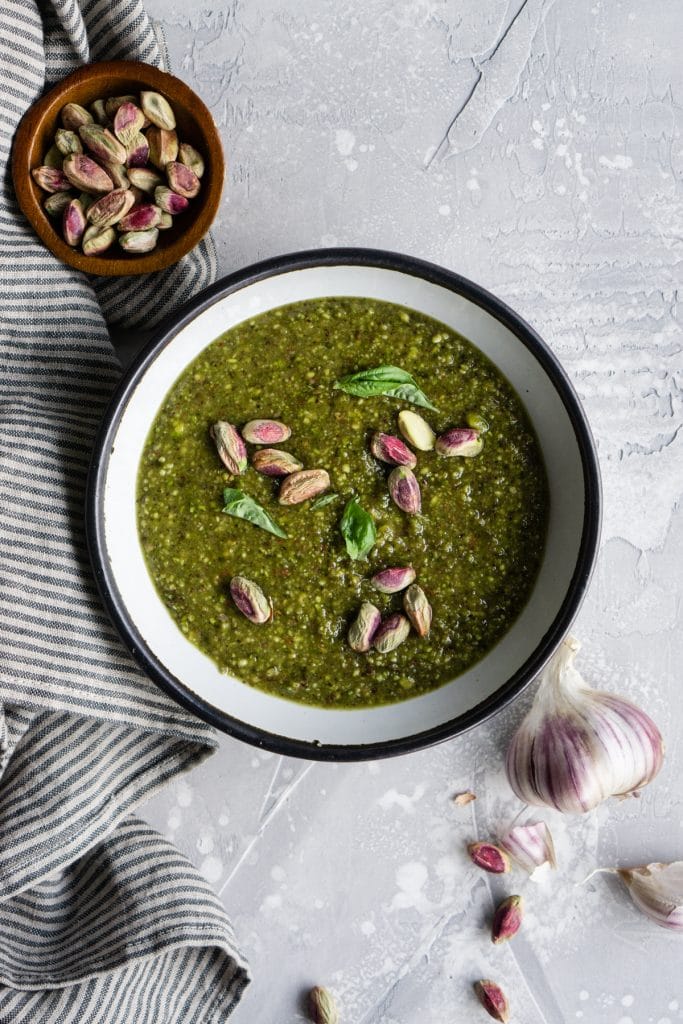 Bowl of pistachio pesto topped with pistachios and fresh basil