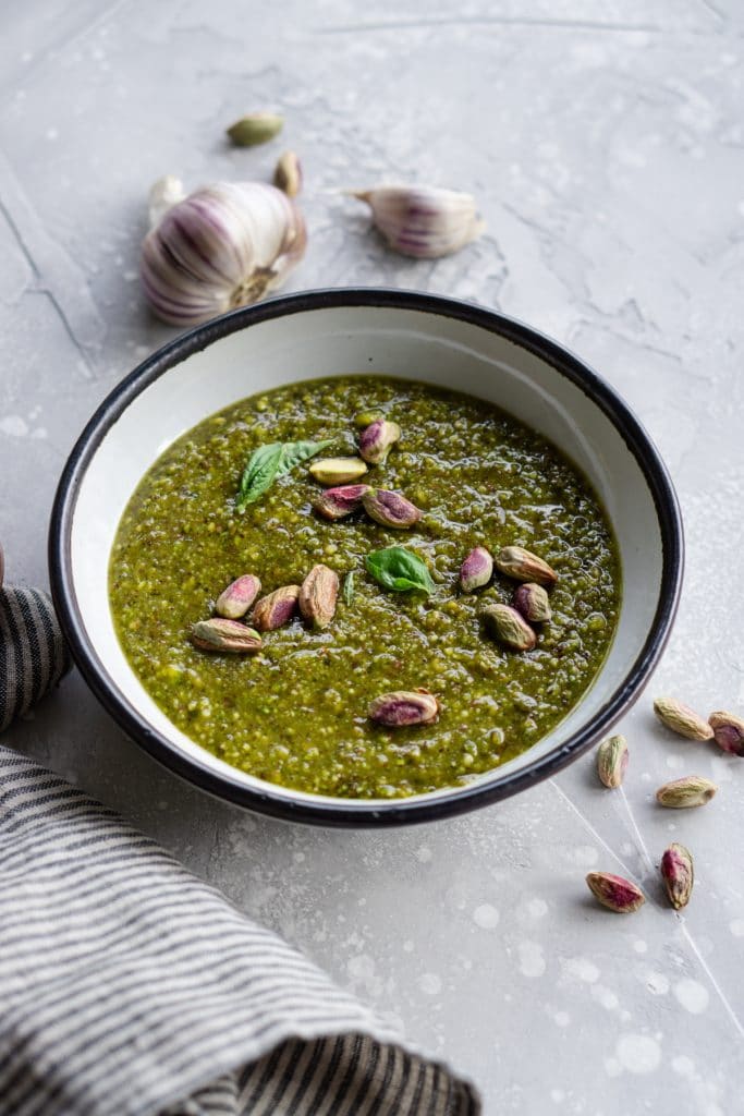 Bowl of pistachio pesto with garlic in the background