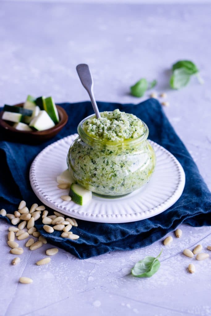 Zucchini pesto in a glass jar on a white plate