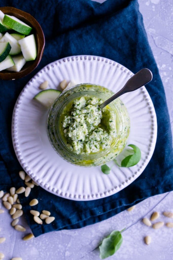 Overhaead shot of zucchini pesto in a glass jar on a white plate
