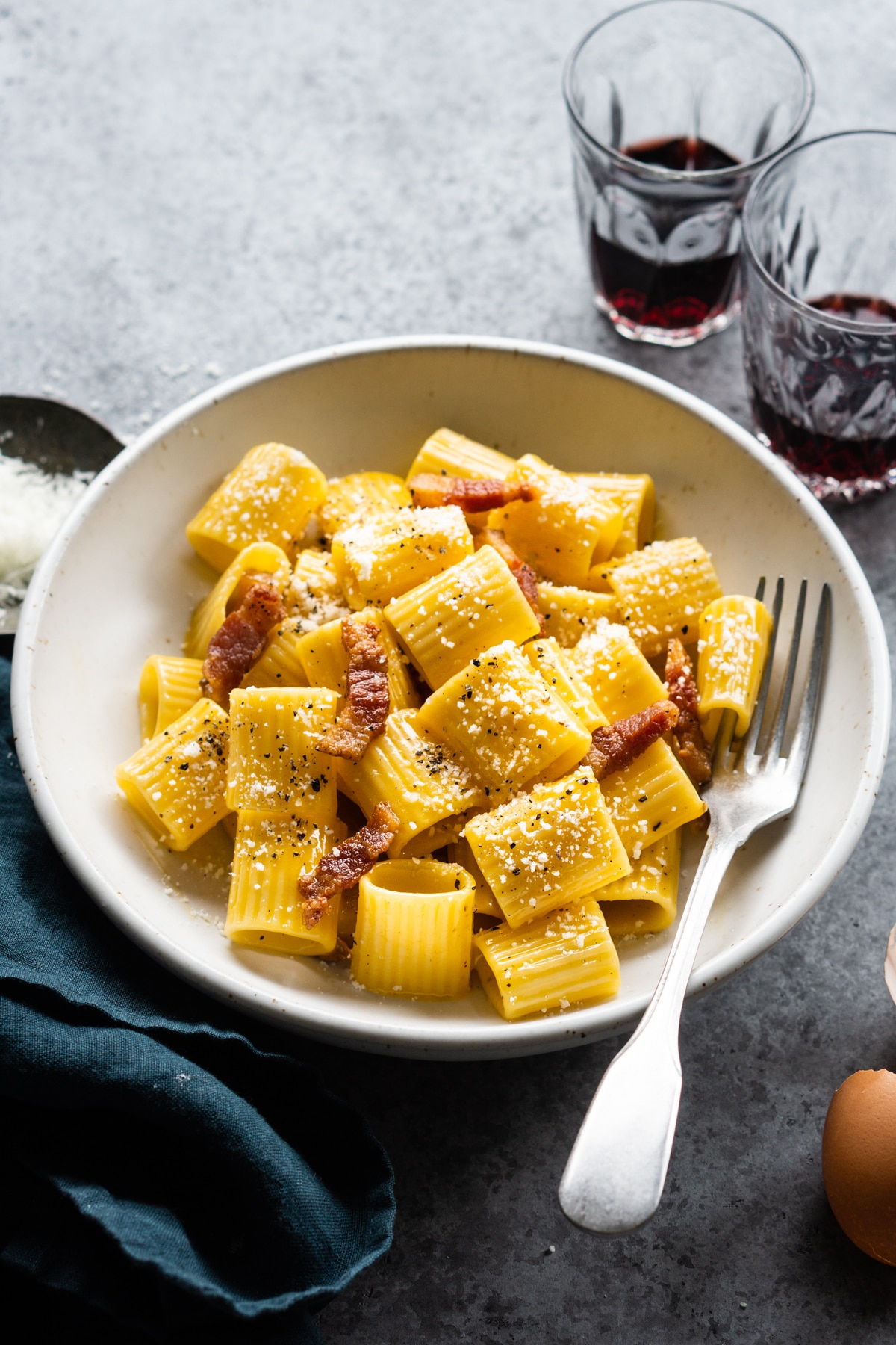 bowl of authentic carbonara pasta with two red wine glasses in the background