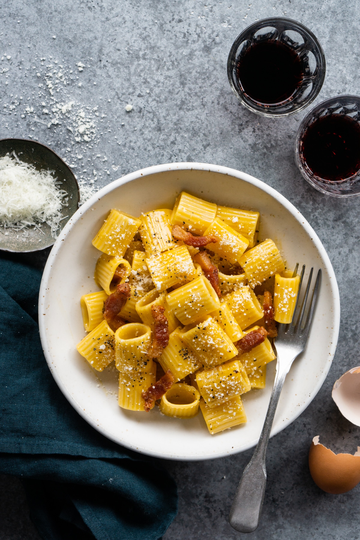 authentic carbonara pasta with guanciale in a bowl with a small plate of cheese to the side