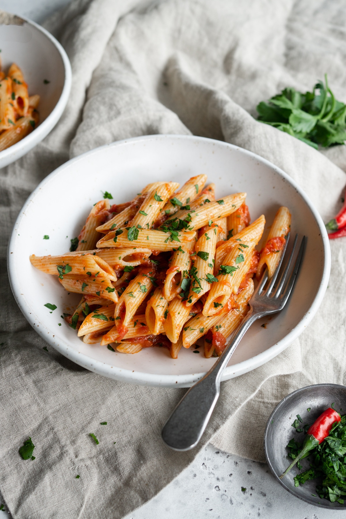 Bowl of penne arrabbiata on a linen napkin with parsley in the background