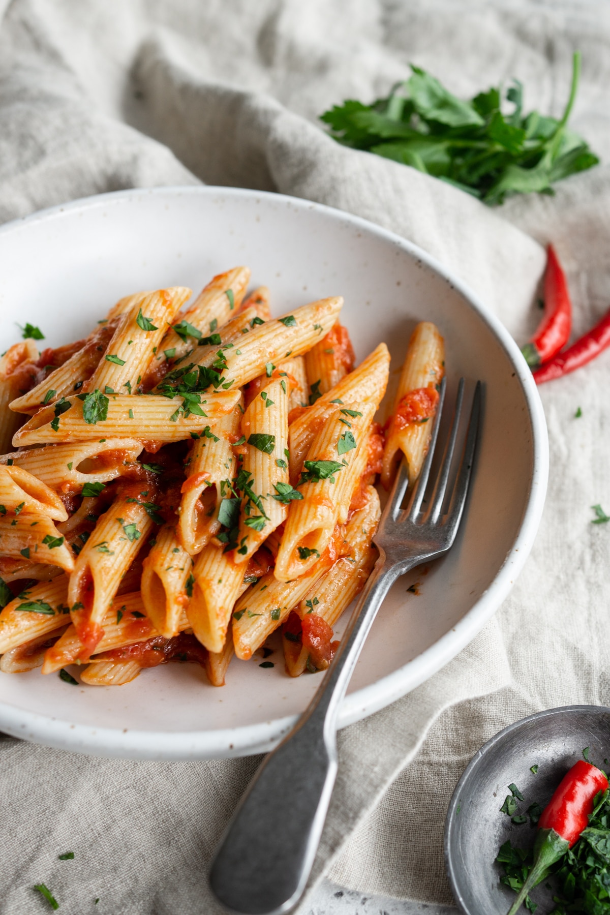 Penne arrabbiata in a bowl with a fork and chili peppers in the background