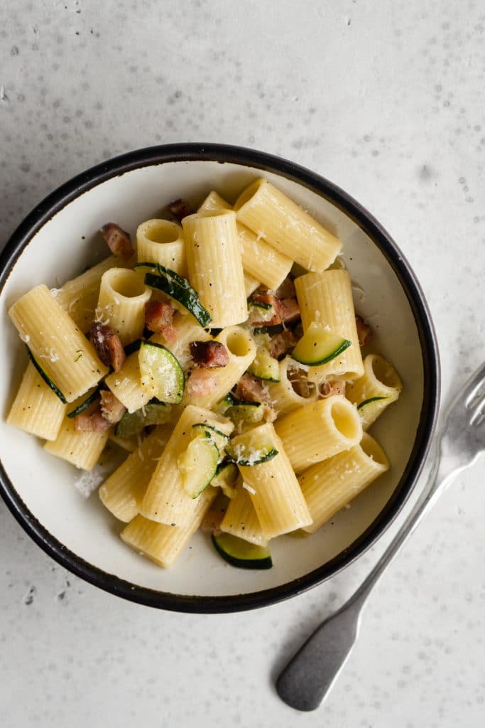 Zucchini and pancetta pasta in a bowl with a fork to the side