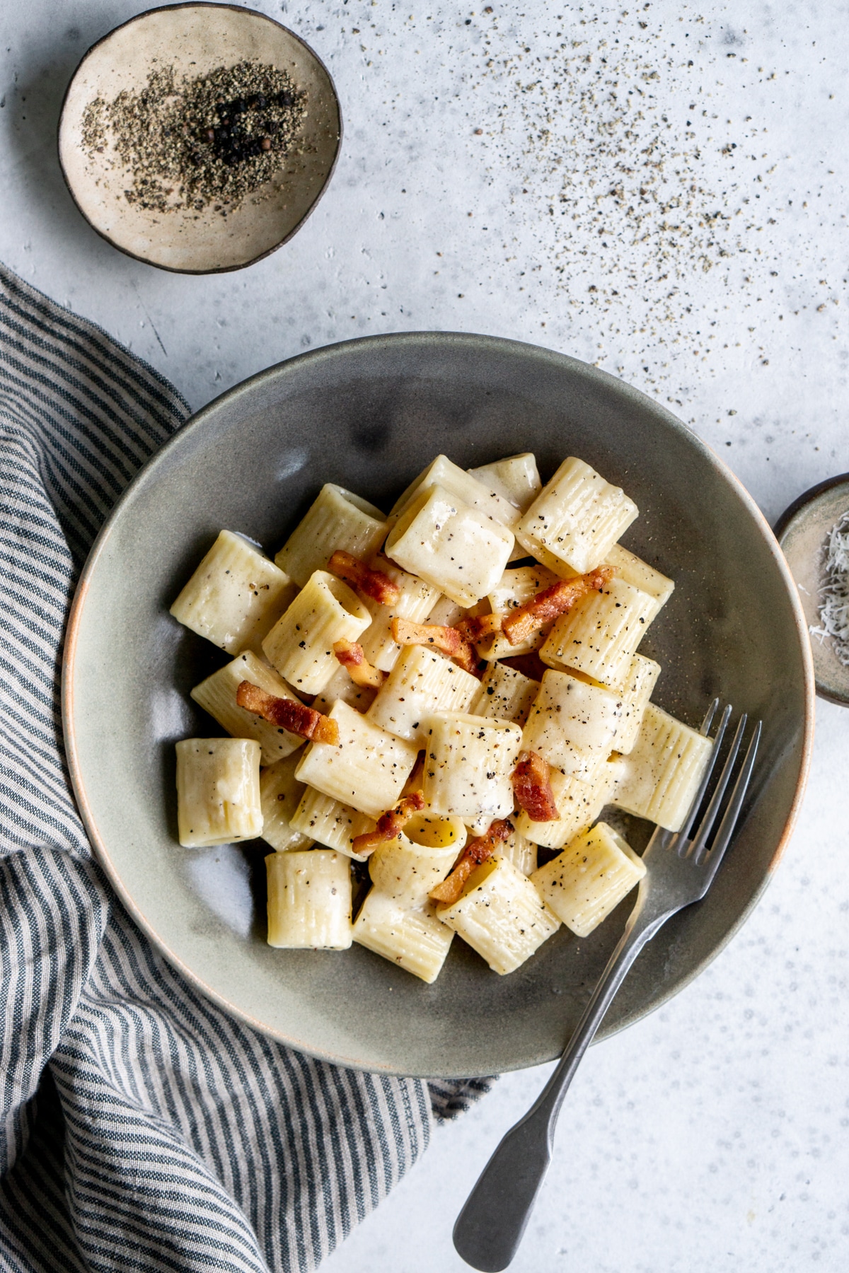 Gricia pasta in a dish with a small bowl of pepper on top