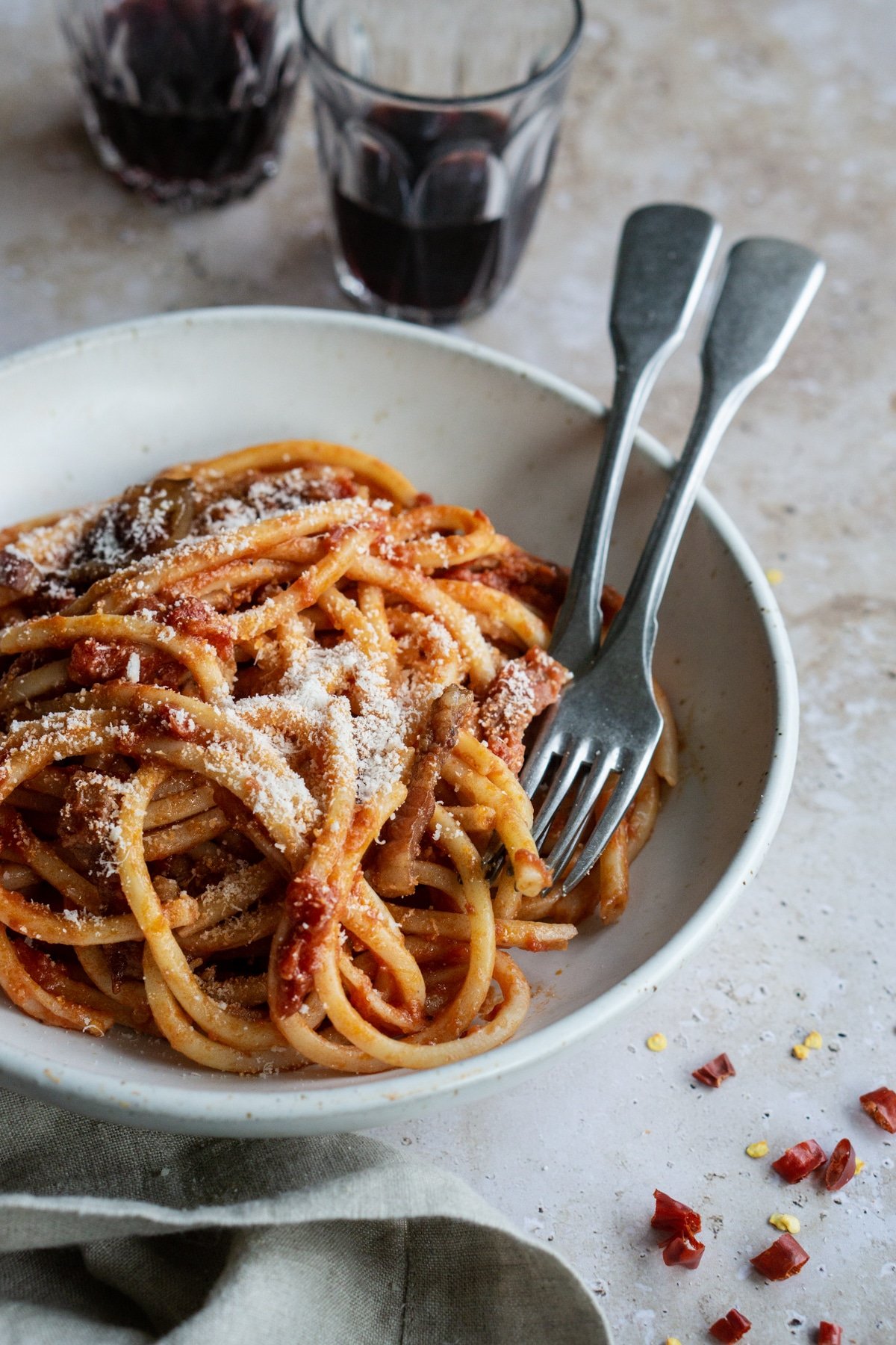 Pasta amatriciana in a bowl with glasses of red wine in the background
