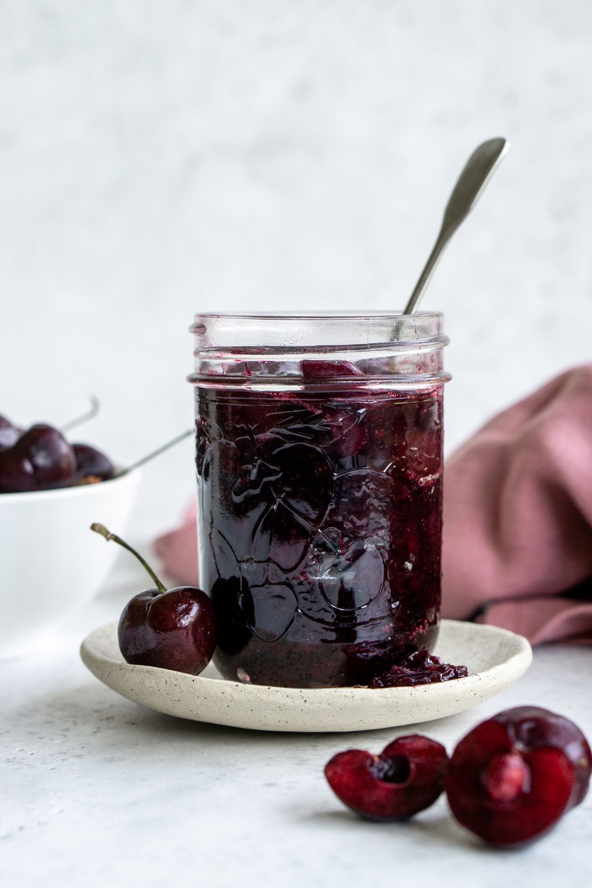 Cherry sauce in a glass jar with a bowl of cherries in the background