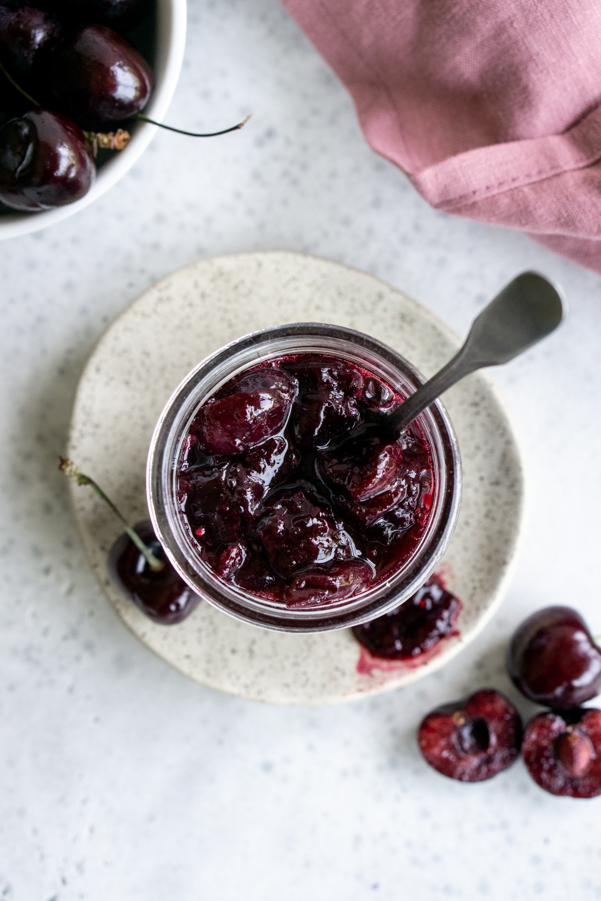 Overhead view of cherry sauce in a glass jar surrounded by cherries