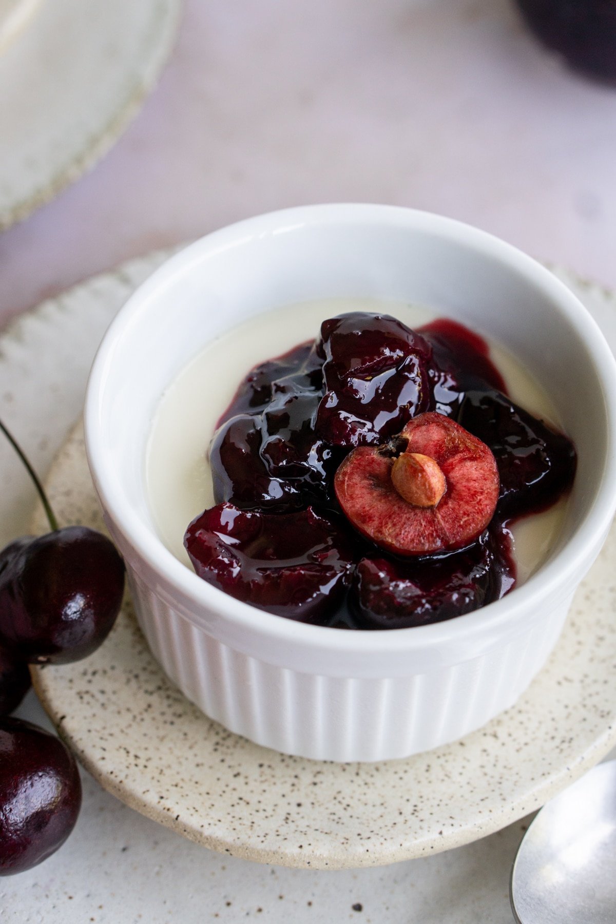 Italian panna cotta in a ramekin, sitting on a plate topped with fresh cherry sauce