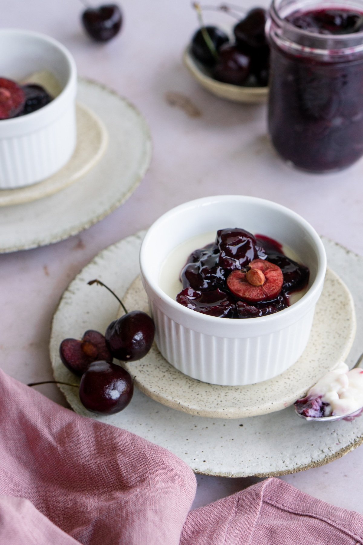 Italian panna cotta in a ramekin surrounded by fresh cherries and a pink napkin
