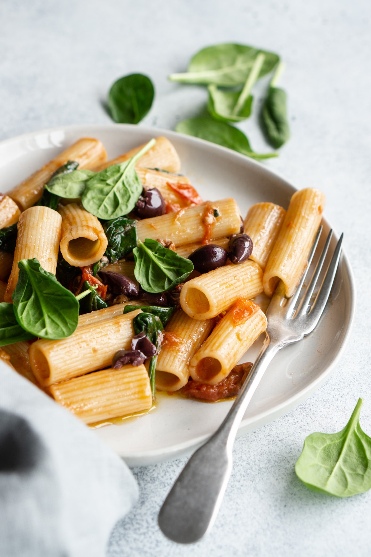 Plate of spinach penne pasta with fresh spinach in the background