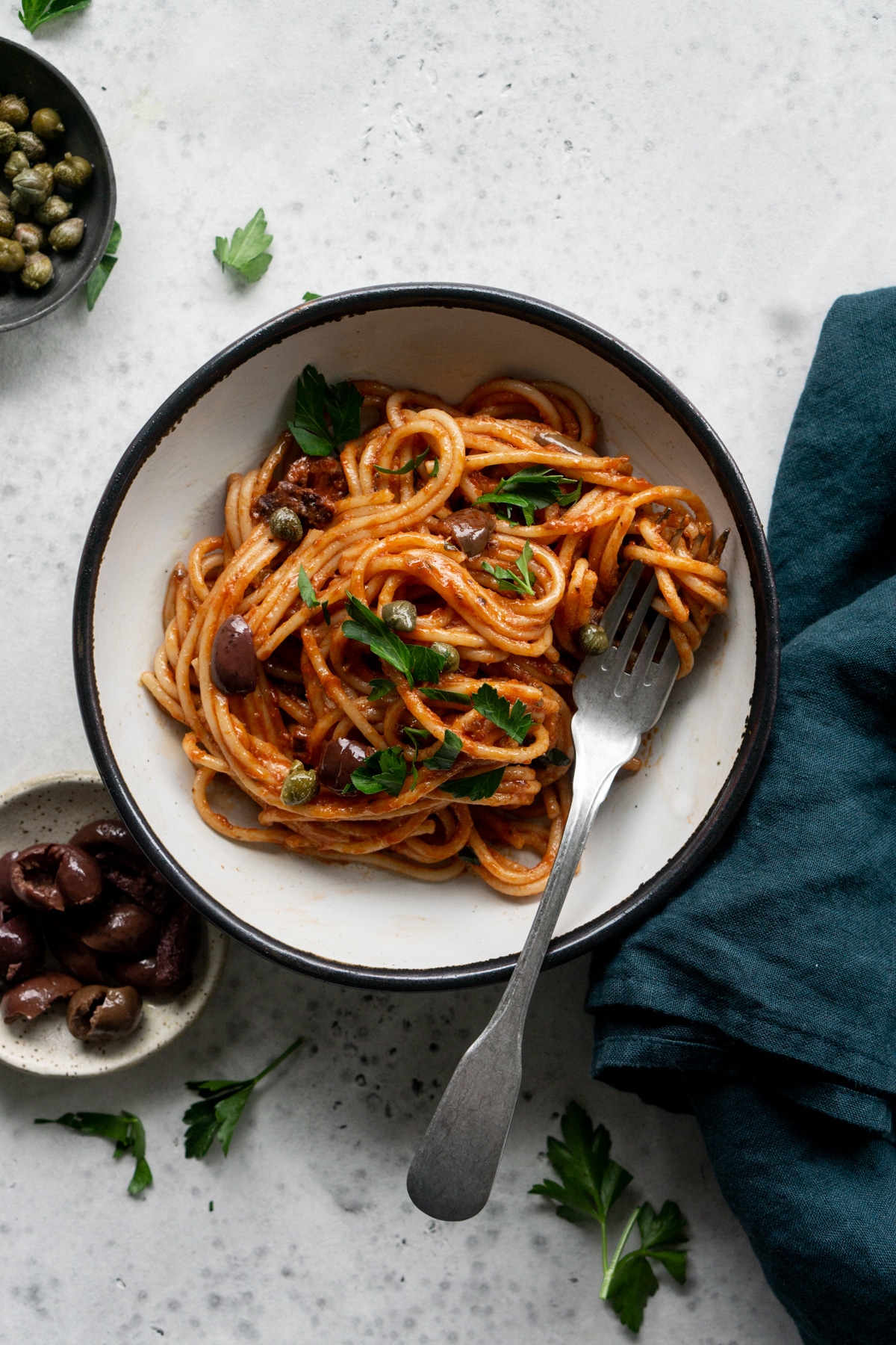 Spaghetti alla puttanesca in a bowl with olives and capers to the side