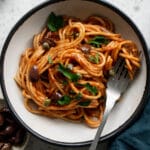 Dish of spaghetti alla puttanesca topped with olives, capers and parsley,with a fork in it