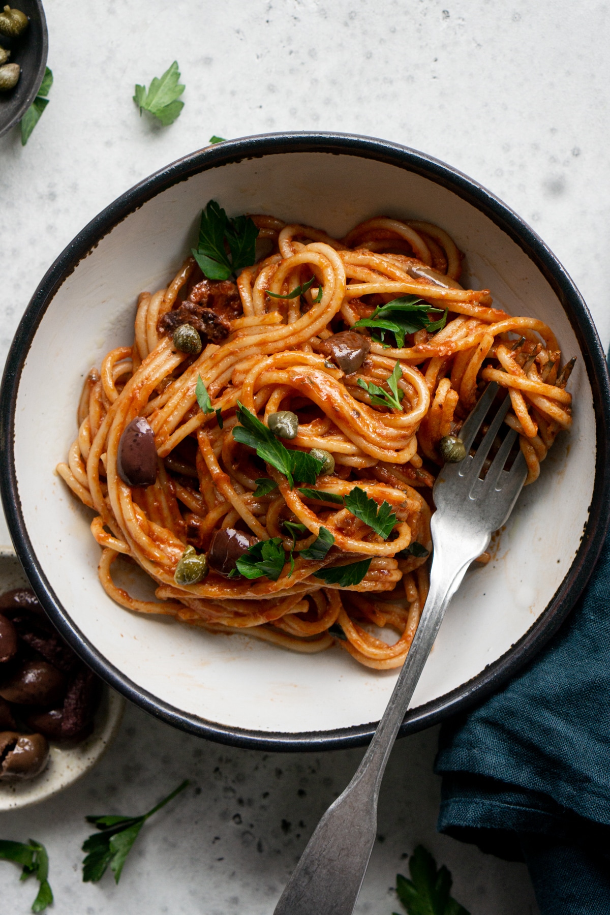 Dish of spaghetti alla puttanesca topped with olives, capers and parsley,with a fork in it