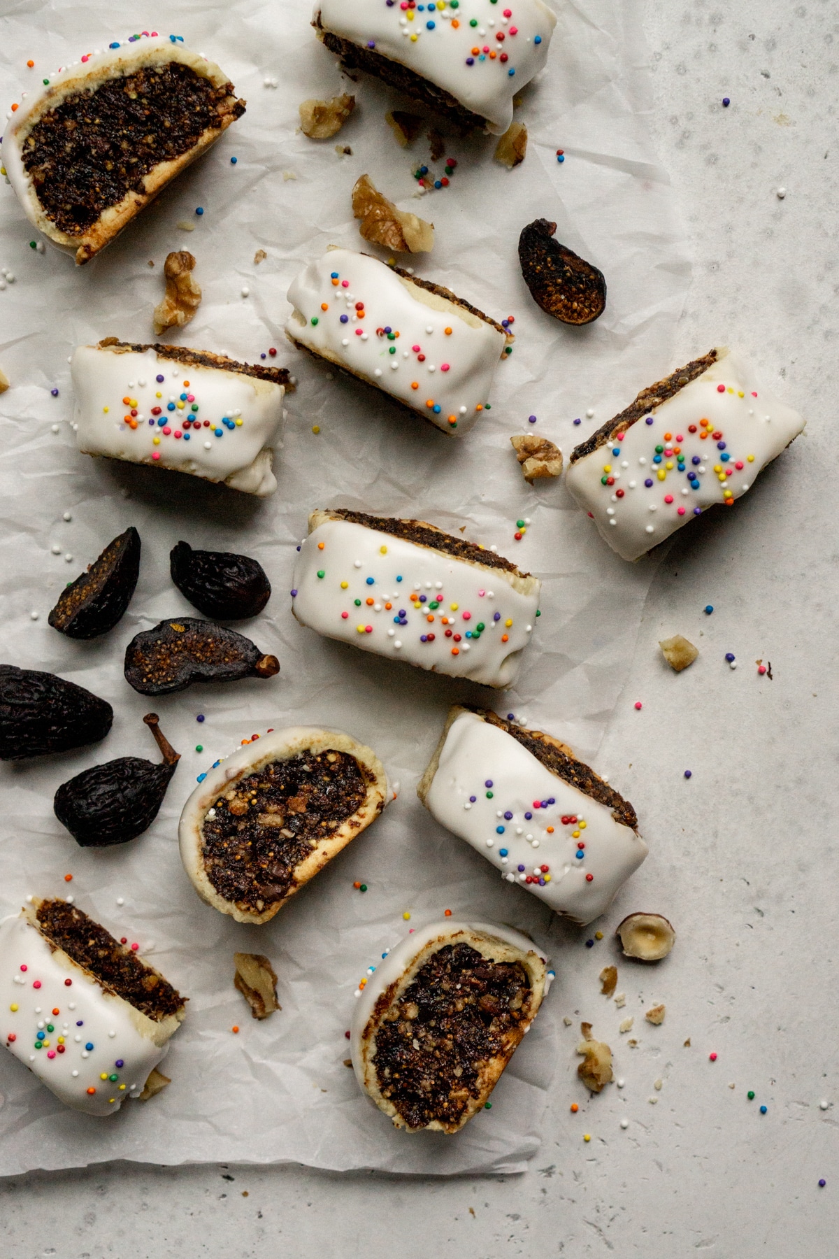 Multiple cuccidati Italian fig cookies on parchment paper surrounded by figs and nuts paper