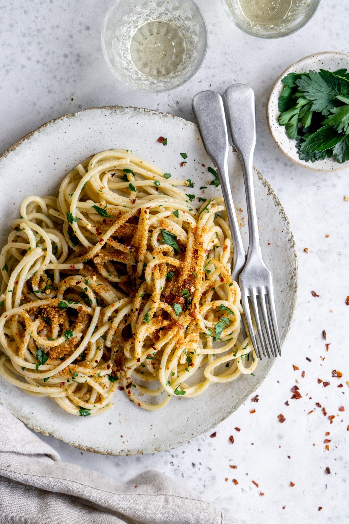 Plate of Italian pasta with anchovies with a fork in it and chili peppers and parsley to the side
