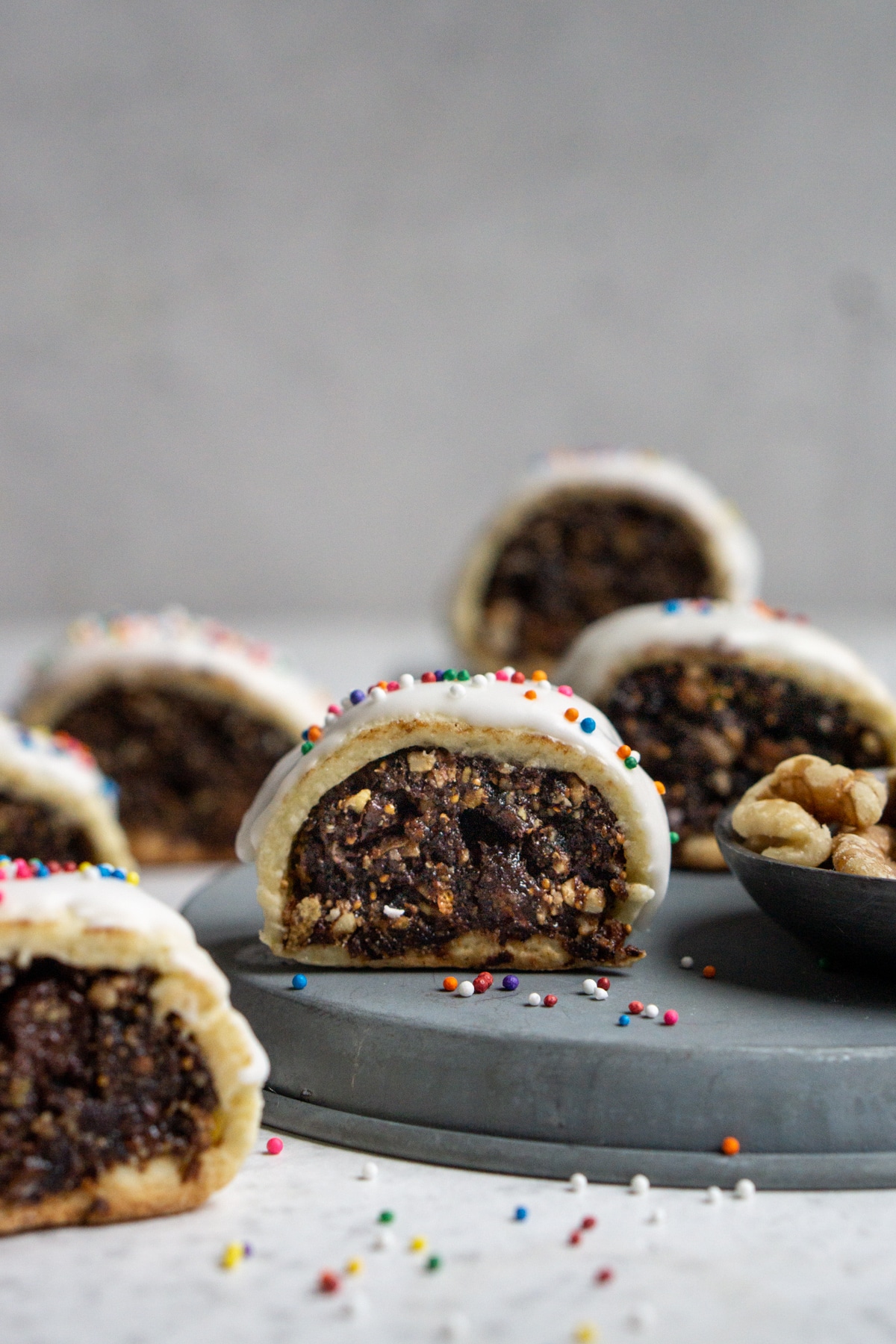 Cuccidati (Italian fig cookies) on a plate surrounded by sprinkles and walnuts