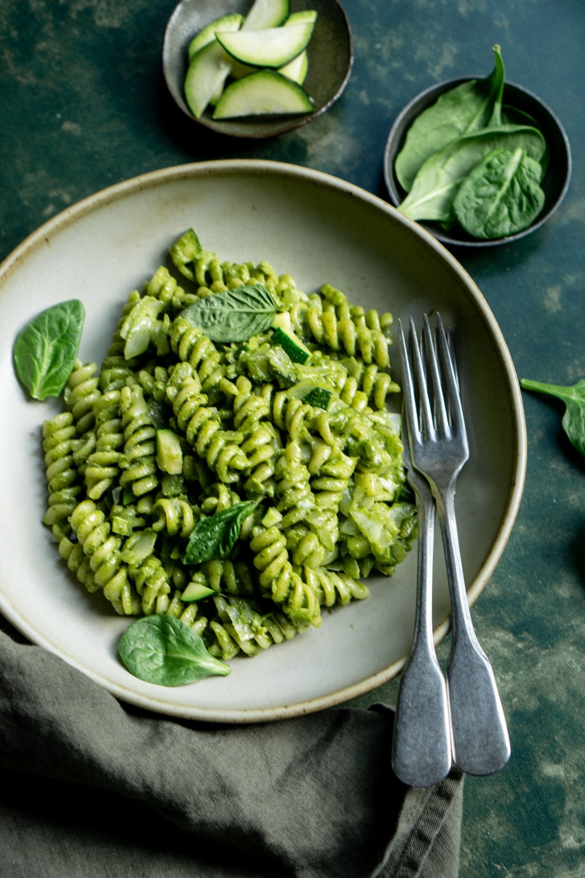 Plate of green goddess pasta with little bowls of zucchini and spinach in the background