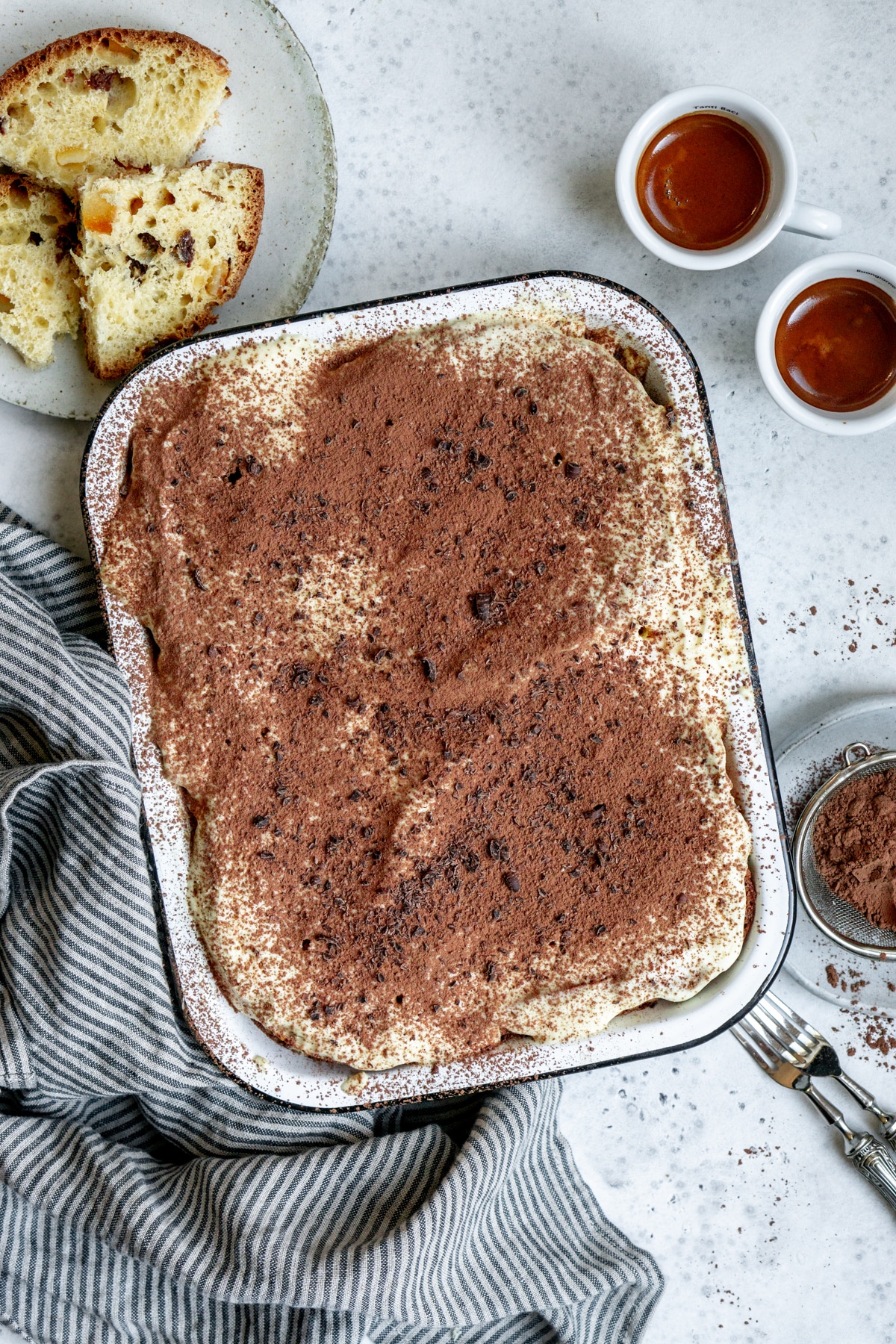 panettone tiramisu in a baking dish with a napkin to the side, and two espressos